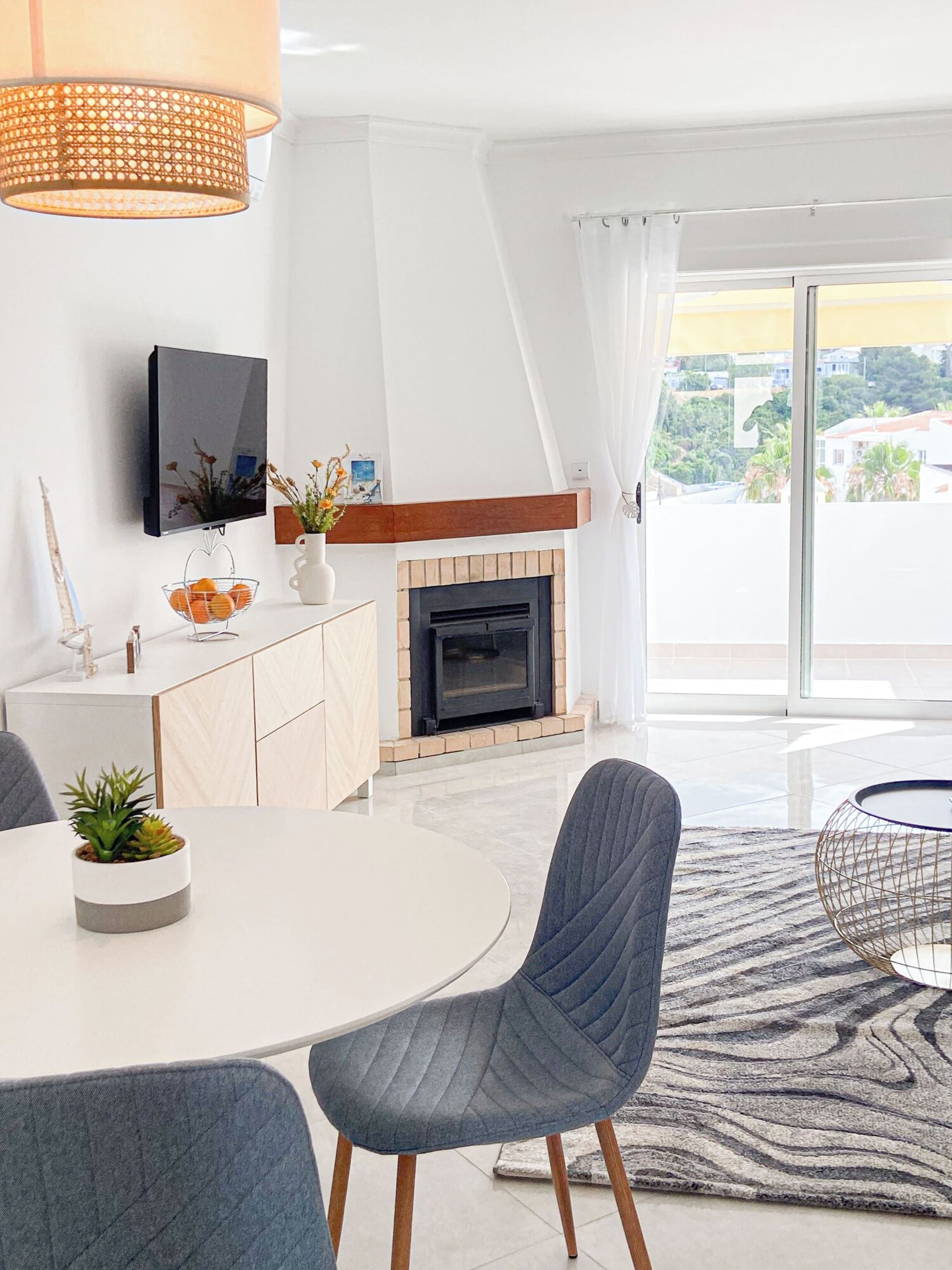 A modern living room with a fireplace, a flat-screen TV, and a dining area with a round table and chairs.