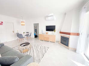 A modern living room with a sofa, dining table, chairs, a TV, and a fireplace. - Casa Joao (Carvoeiro)