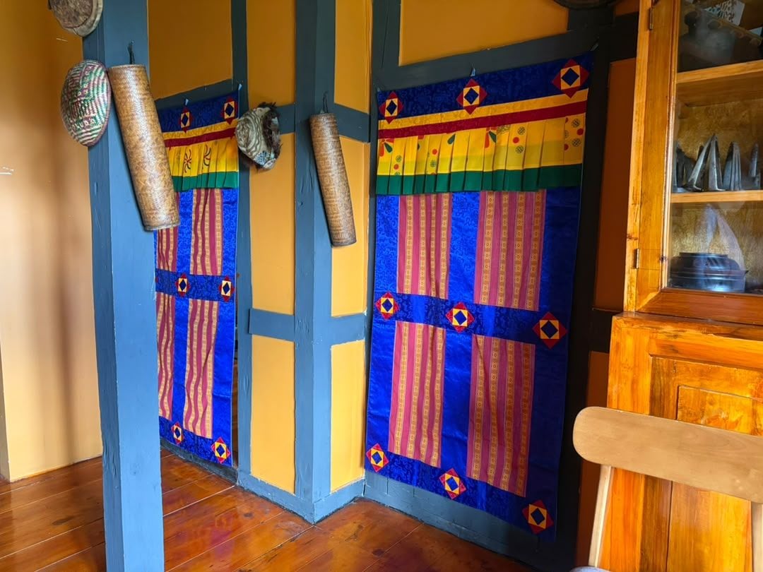 Une pièce avec un plancher en bois, une porte bleue ornée d’une courtepointe aux couleurs vives, et un meuble en bois doté de portes en verre.