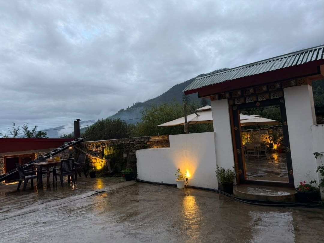 Un patio techado al aire libre con una mesa, sillas, una escalera y una vista de la montaña al fondo.