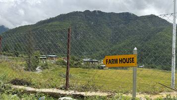 A fenced area with a sign indicating a farm house, surrounded by greenery and a mountain backdrop.