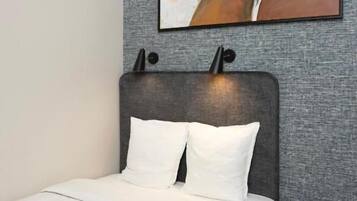 Un dormitorio con cama, cabecera, un cuadro en la pared y una mesita redonda.