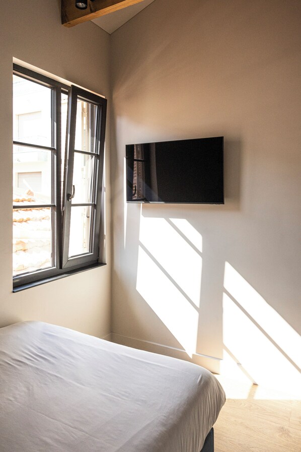 A bedroom with a bed, a window, and a wall-mounted television.