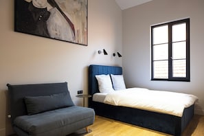 A bedroom with a bed, a sofa, a painting, and a window.