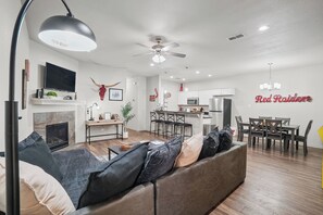 A modern living room with a fireplace, a dining area, and a kitchen. - Double T Rally House - 3BR/3BA - Walk to Tech (Lubbock)