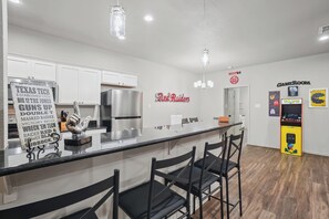 A modern kitchen with a bar area, white cabinets, stainless steel appliances, and a 'Red Raiders' sign on the wall. - Double T Rally House - 3BR/3BA - Walk to Tech (Lubbock)