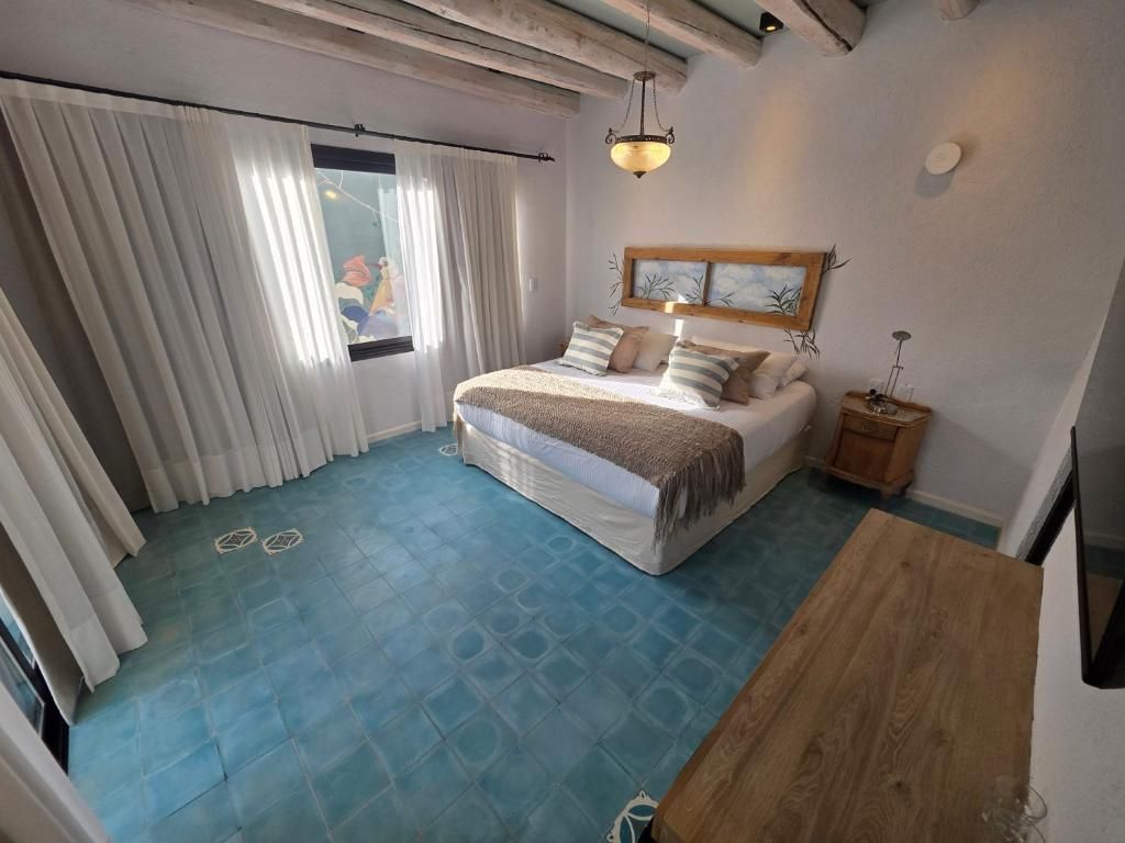 Un dormitorio con cama, cortinas, una mesita de noche de madera y televisor montado en la pared.