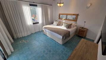 Un dormitorio con cama, cortinas, una mesita de noche de madera y televisor montado en la pared.