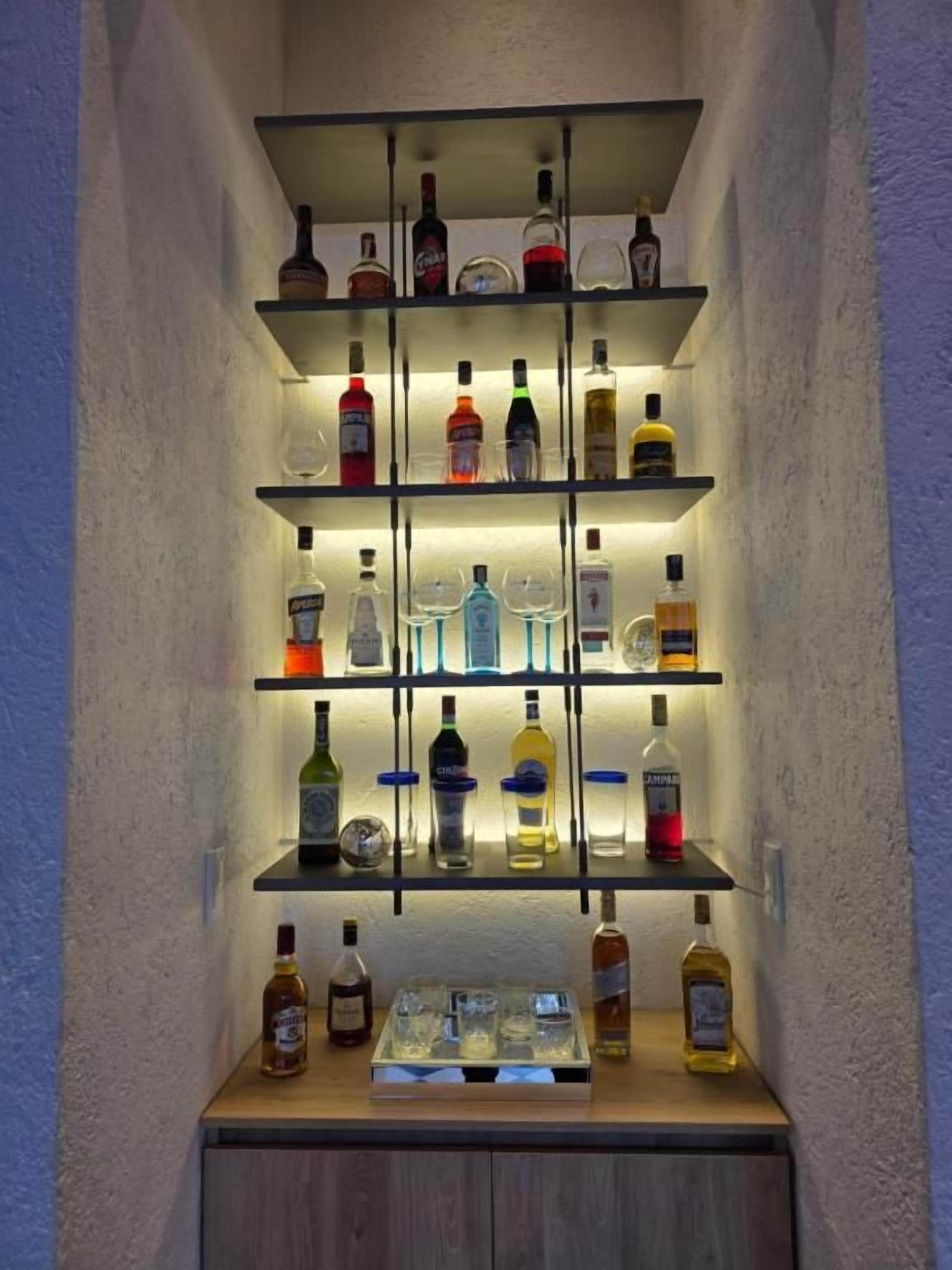 Un espace bar avec des étagères remplies de bouteilles d’alcool et de verres.