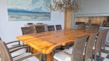 Un comedor con una gran mesa de madera rodeada de sillas de mimbre, un cuadro en la pared y una lámpara de araña moderna.