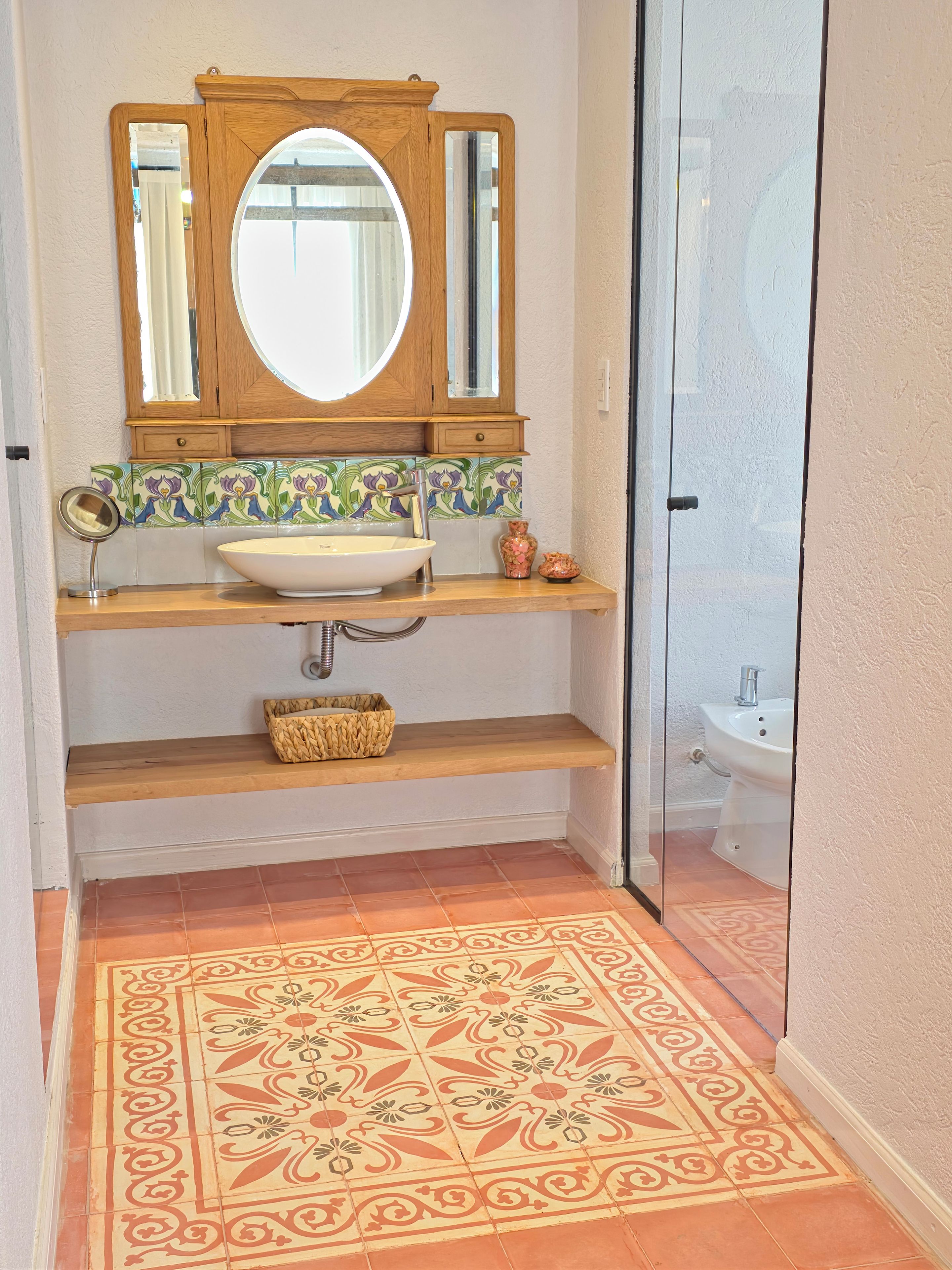 A bathroom with a wooden vanity, a round mirror, a vessel sink, and a patterned floor.