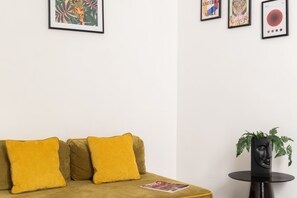 Ein Zimmer mit einer Couch, einem kleinen runden Tisch mit einer Pflanze und gerahmten Kunstwerken an der Wand.