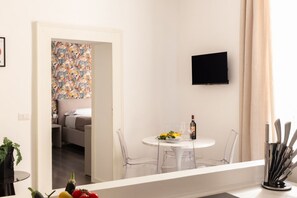 A modern dining area with a round table, clear chairs, a bottle of wine, and a fruit plate. A flat-screen TV is mounted on the wall. - La Casa di Renato | 2BR in the heart of Sorrento (Sorrento)