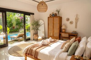 Een slaapkamer met een bed, nachtkastje, lamp, kledingkast en uitzicht op een zwembad en tuin.