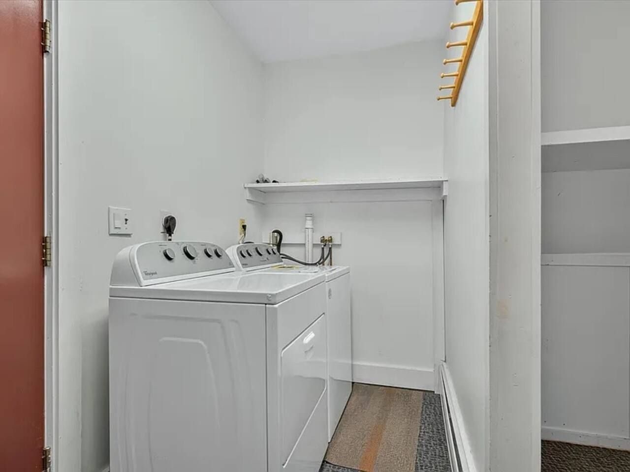 Ein Waschraum mit einer Frontlader-Waschmaschine und einem Trockner, einem Regal über dem Trockner und einem Holzgestell an der Wand.