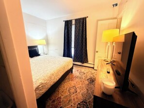 A hotel room with a bed, a bathroom with a mirror, and a window with curtains. - Modern 3BR/2BA | 3 Min to Okemo Mountain (Ludlow)