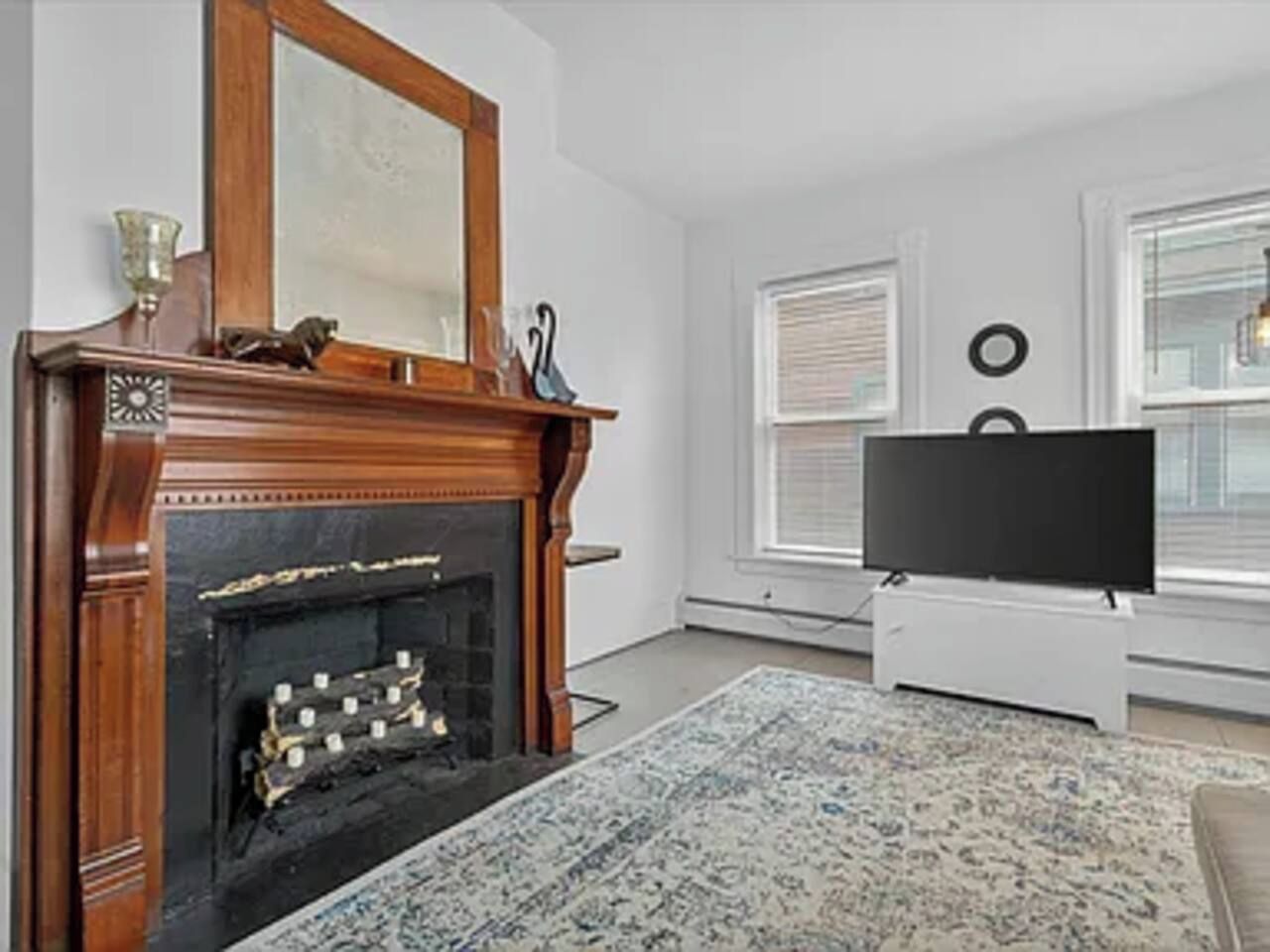 A living room with a fireplace, a television, and a window with blinds.