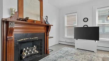 A living room with a fireplace, a television, and a window with blinds.