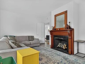 A living room with a fireplace, a sofa, and a yellow side table. - Modern 3BR/2BA | 3 Min to Okemo Mountain (Ludlow)