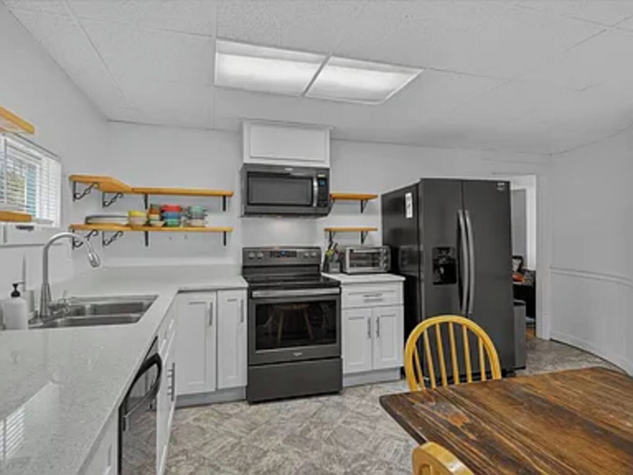 A kitchen with white cabinets, a microwave, a stove, a refrigerator, and a wooden dining table.
