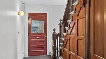 A hallway with a red door, a wooden staircase, and a wall-mounted light fixture.