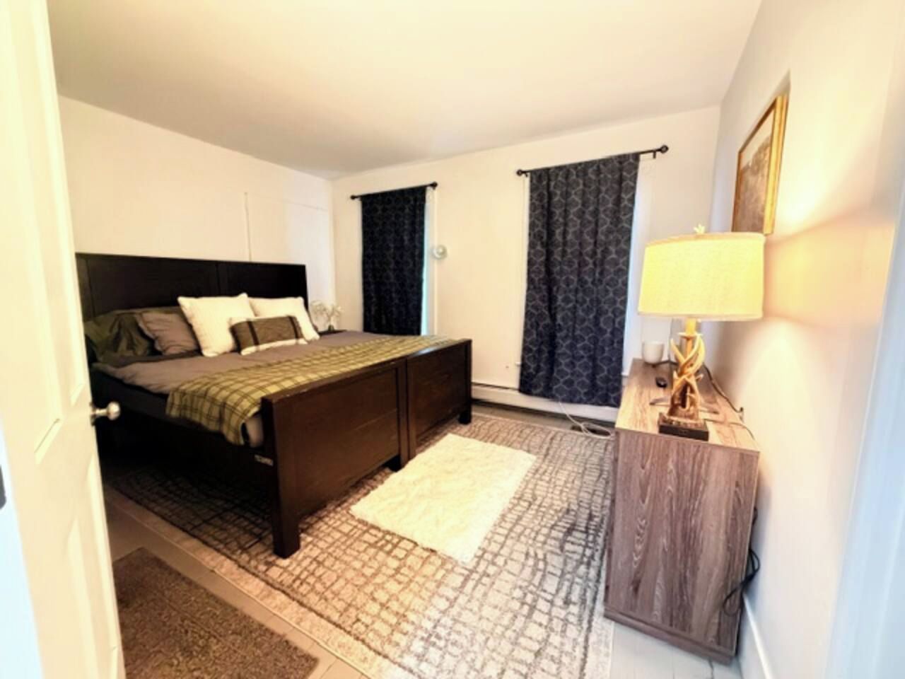 A bedroom with a bed, bedside table, lamp, and curtains.