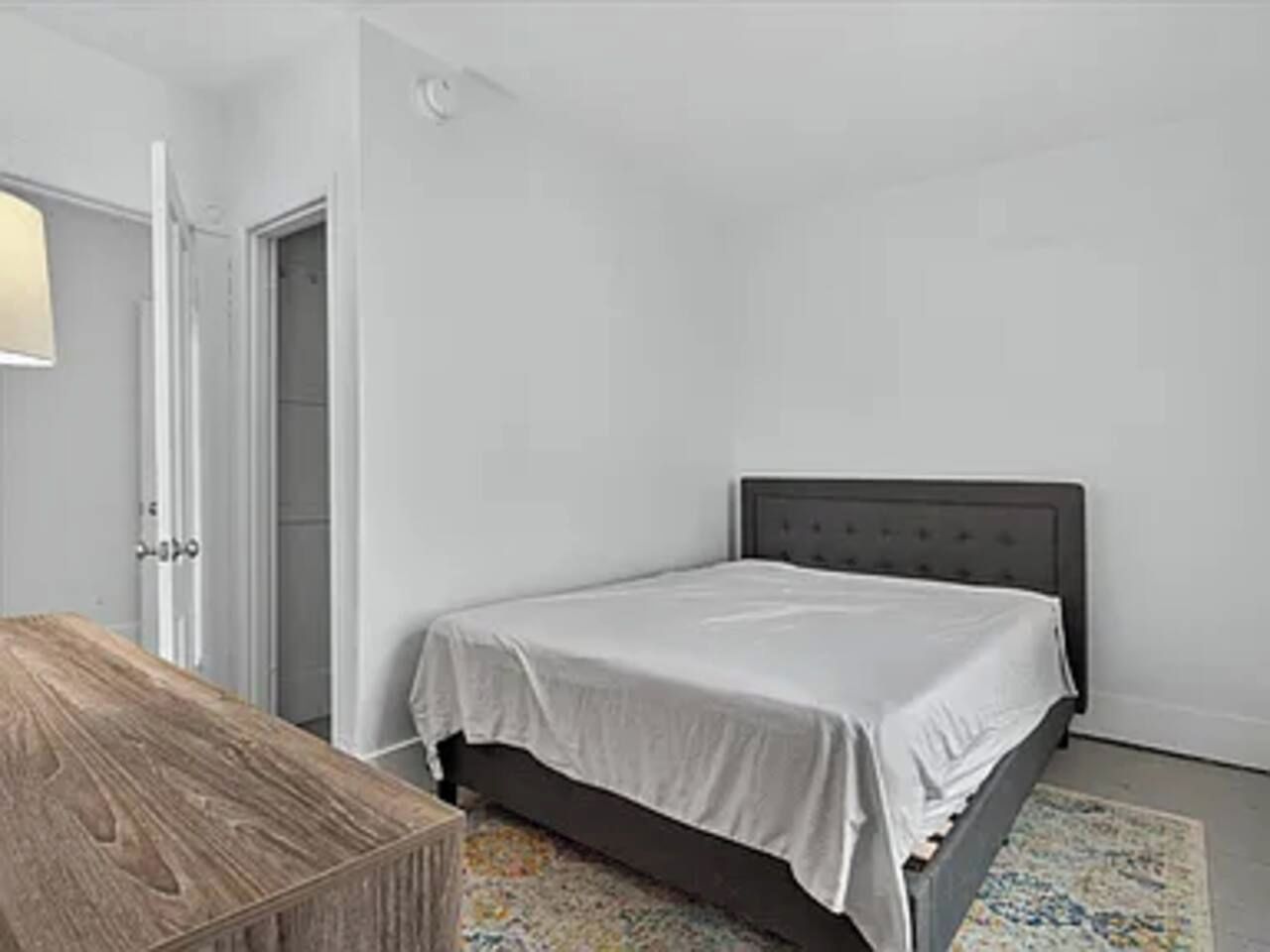 Une chambre à coucher avec un lit, une table de chevet en bois et une porte.