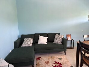 Ein Wohnzimmer mit einem grünen Sofa, einem gemusterten Teppich und einem kleinen Tisch mit Bilderrahmen.