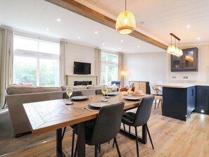Ein moderner Essbereich mit Holztisch, schwarzen Stühlen und einer Couch im Hintergrund.
