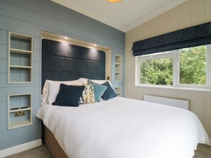 Ein Schlafzimmer mit Bett, Einbauschränken, einem Fenster mit Grünblick und einer Deckenleuchte.