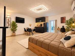 A modern bedroom with a large bed, a dining area with chairs, a kitchen with appliances, and a television on the wall. - Nova Plebiscito 3 One Minute From Plebiscito (Naples)