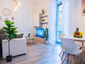 Ein modernes Wohnzimmer mit Fernseher, einem Kaktus und einem Esstisch mit Obst.