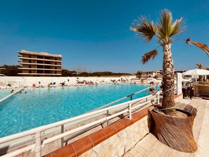 A swimming pool with a palm tree and a building in the background. - Athena Seafront Apartment Parking Pool (Castel Volturno)