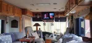 A cozy living area with a sofa, armchairs, a small table, and a television mounted on the wall.