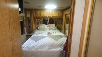 Un pasillo estrecho que conduce a un dormitorio con cama, armarios de madera y un espejo.