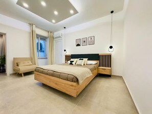 Ein modernes Schlafzimmer mit einem hölzernen Bett, einem Nachttisch, einem Sessel und einem Fenster mit Vorhängen.