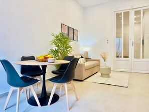 A modern living room with a round dining table, two chairs, a sofa, a potted plant, and a door with glass panels. - Nova Plebiscito 1 Suite in Naples Center (Naples)