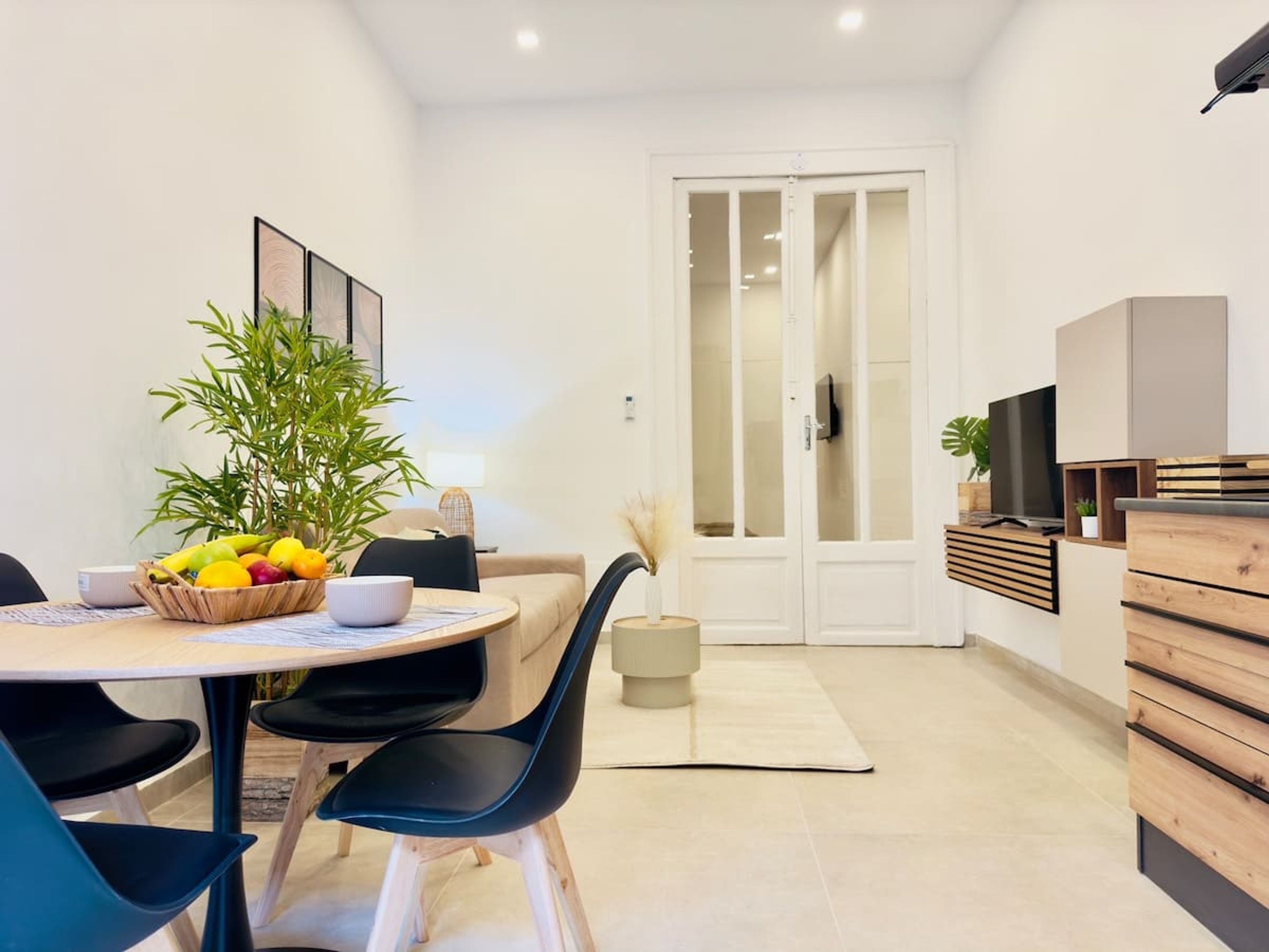 Un comedor moderno con una mesa redonda, sillas negras y una cesta de frutas.