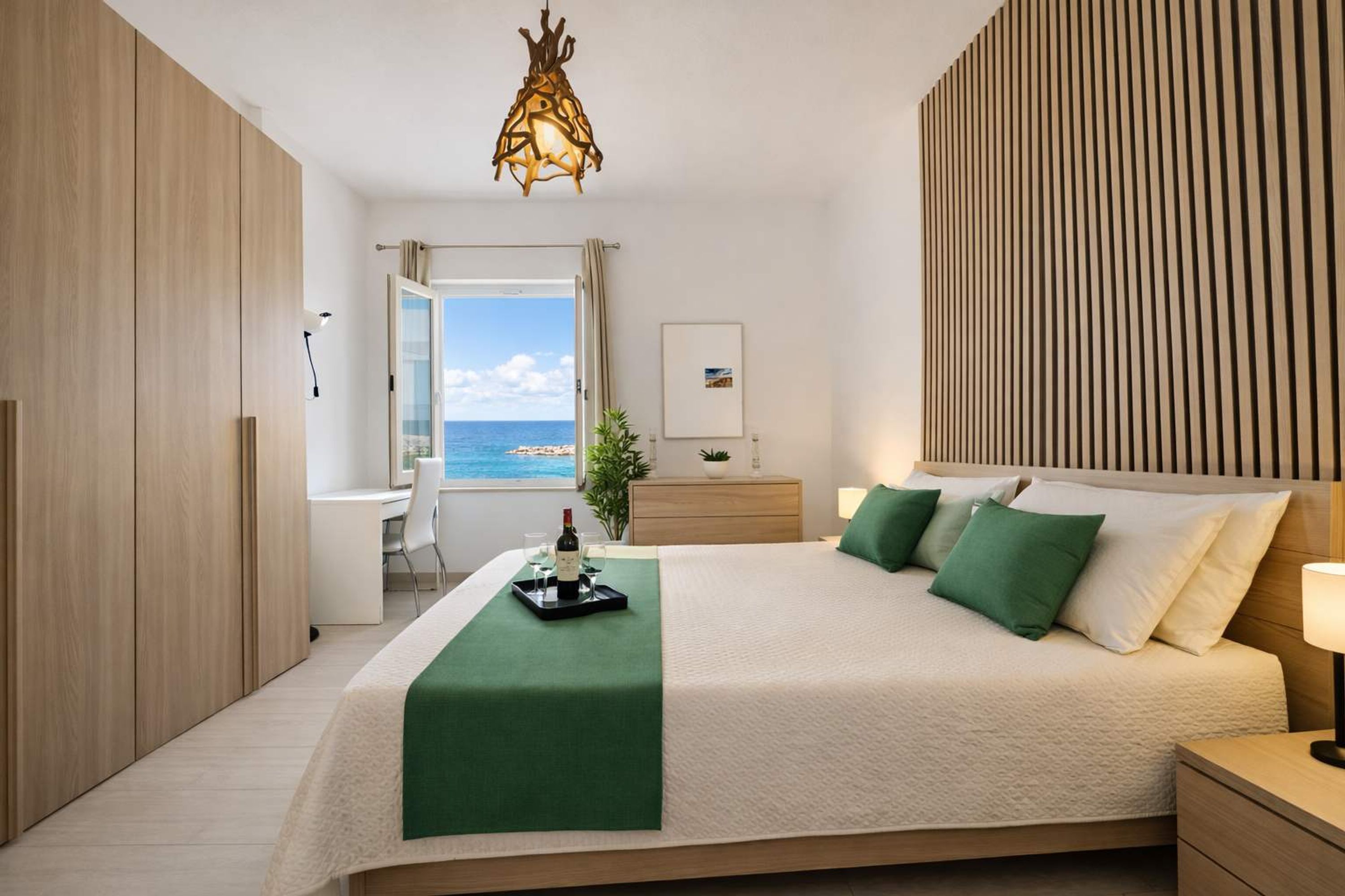 A modern bedroom with a large bed, a view of the sea, and a wooden panel wall.