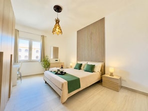 Un dormitorio moderno con cama, mesitas de noche, un escritorio y una lámpara colgante.