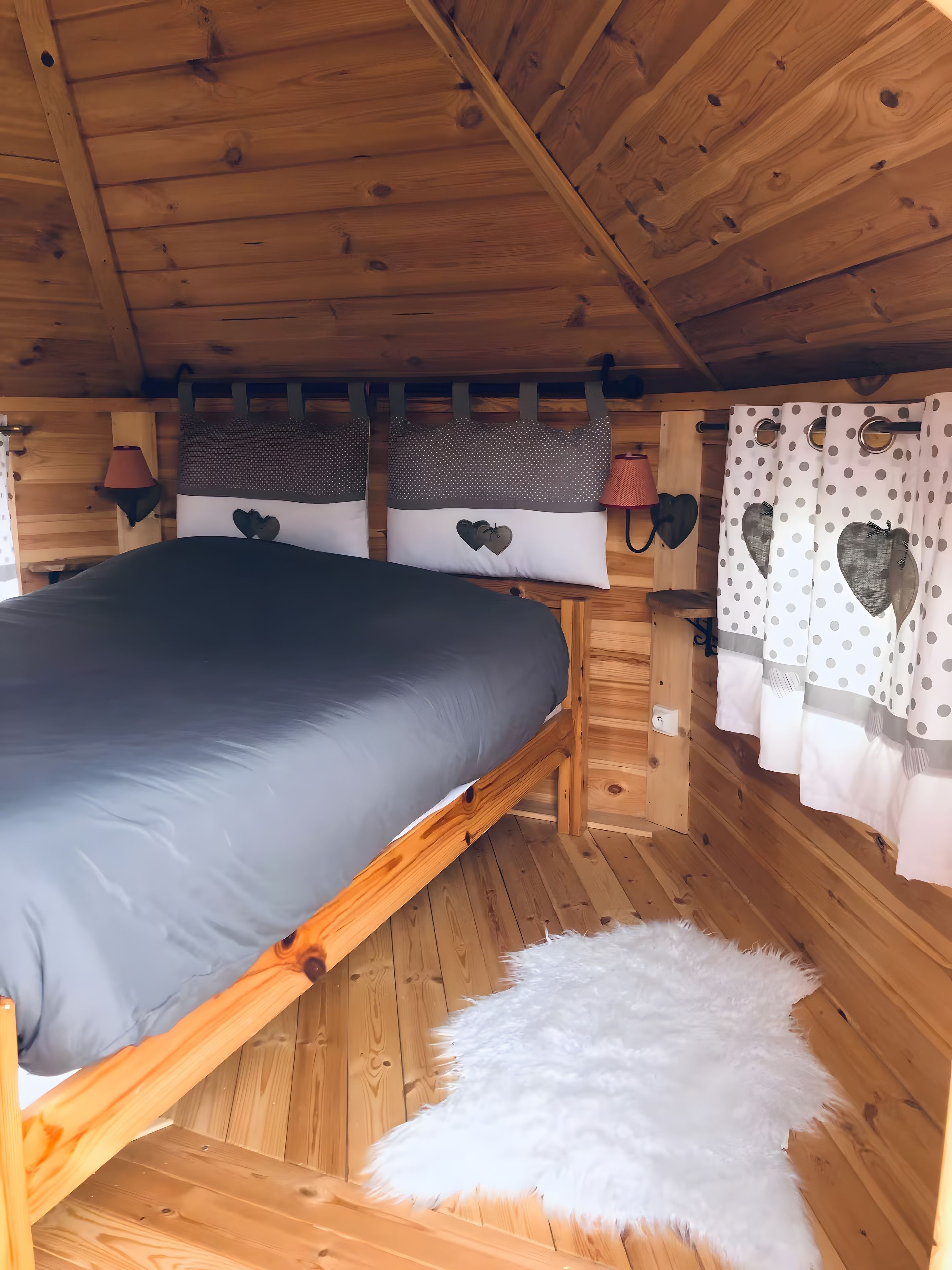 Een slaapkamer in een houten chalet, met een bed, kussens en gordijnen.
