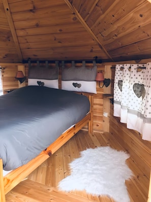 Une chambre dans une cabane en bois, avec un lit, des oreillers et des rideaux.