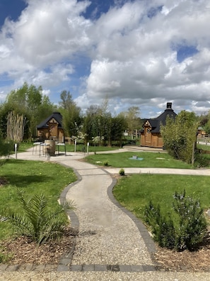 Polku johtaa puisille mökeille, ja taustalla on nurmikkoalue sekä puita.