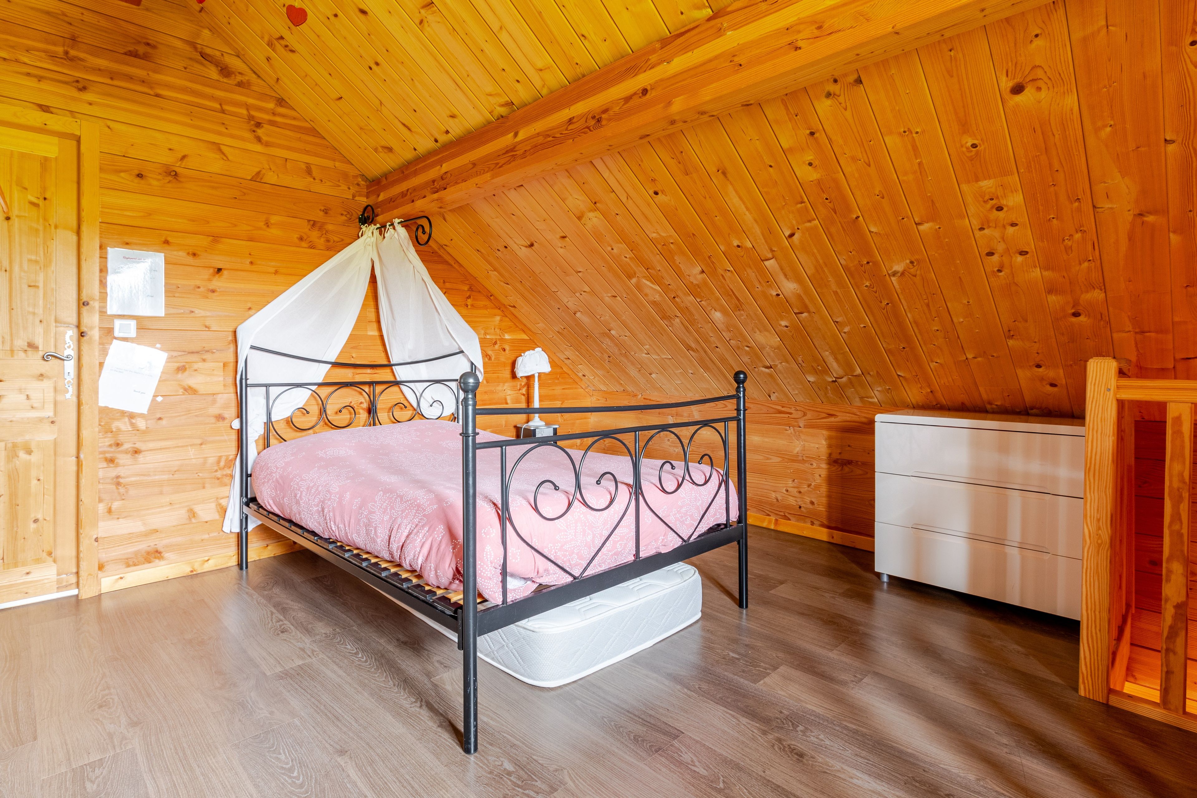 Une chambre à coucher dans une cabane en bois, avec un lit à baldaquin, une table de chevet blanche et une armoire en bois.