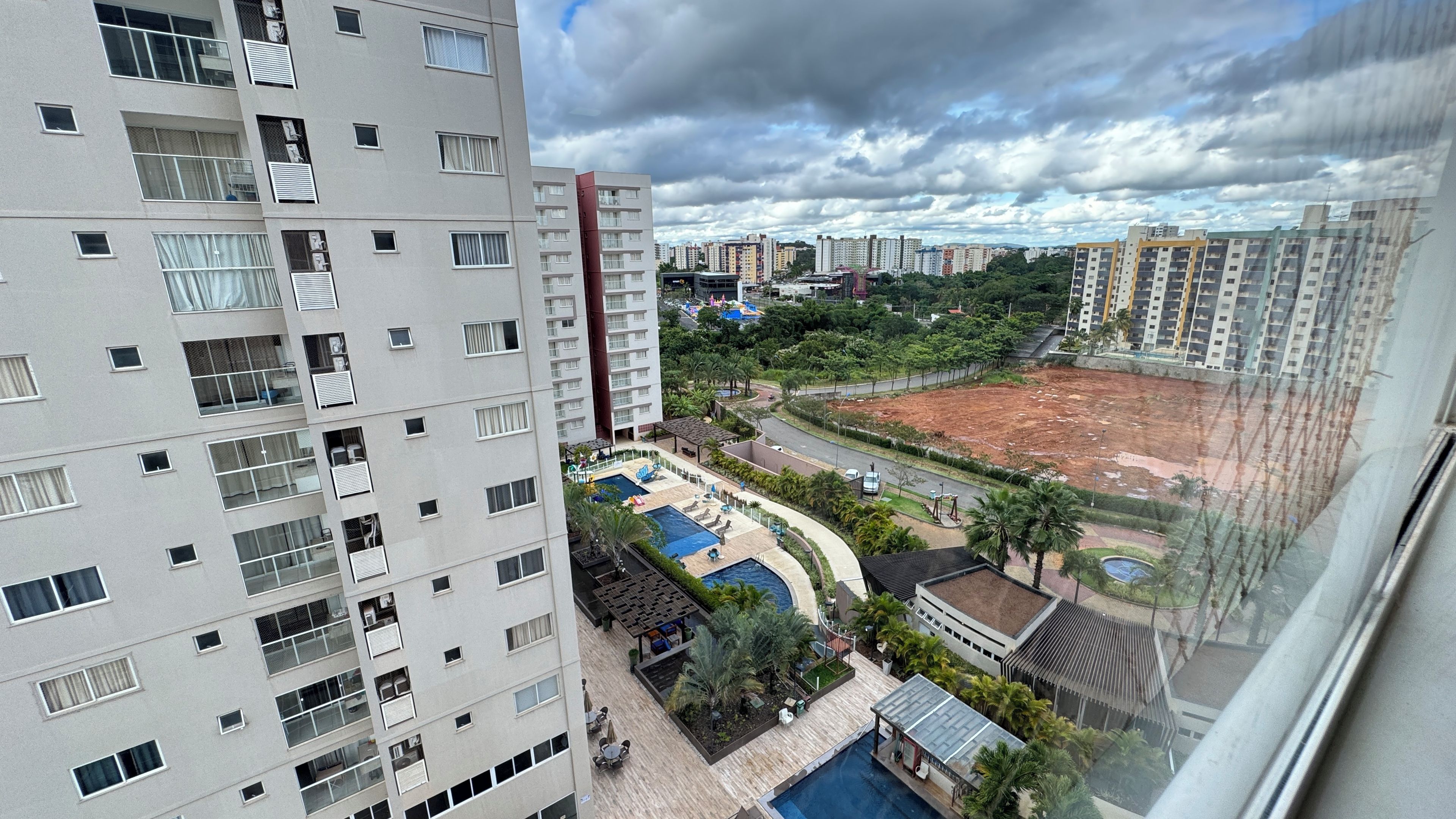A high-rise building with multiple balconies, a swimming pool, and a landscaped area with palm trees.