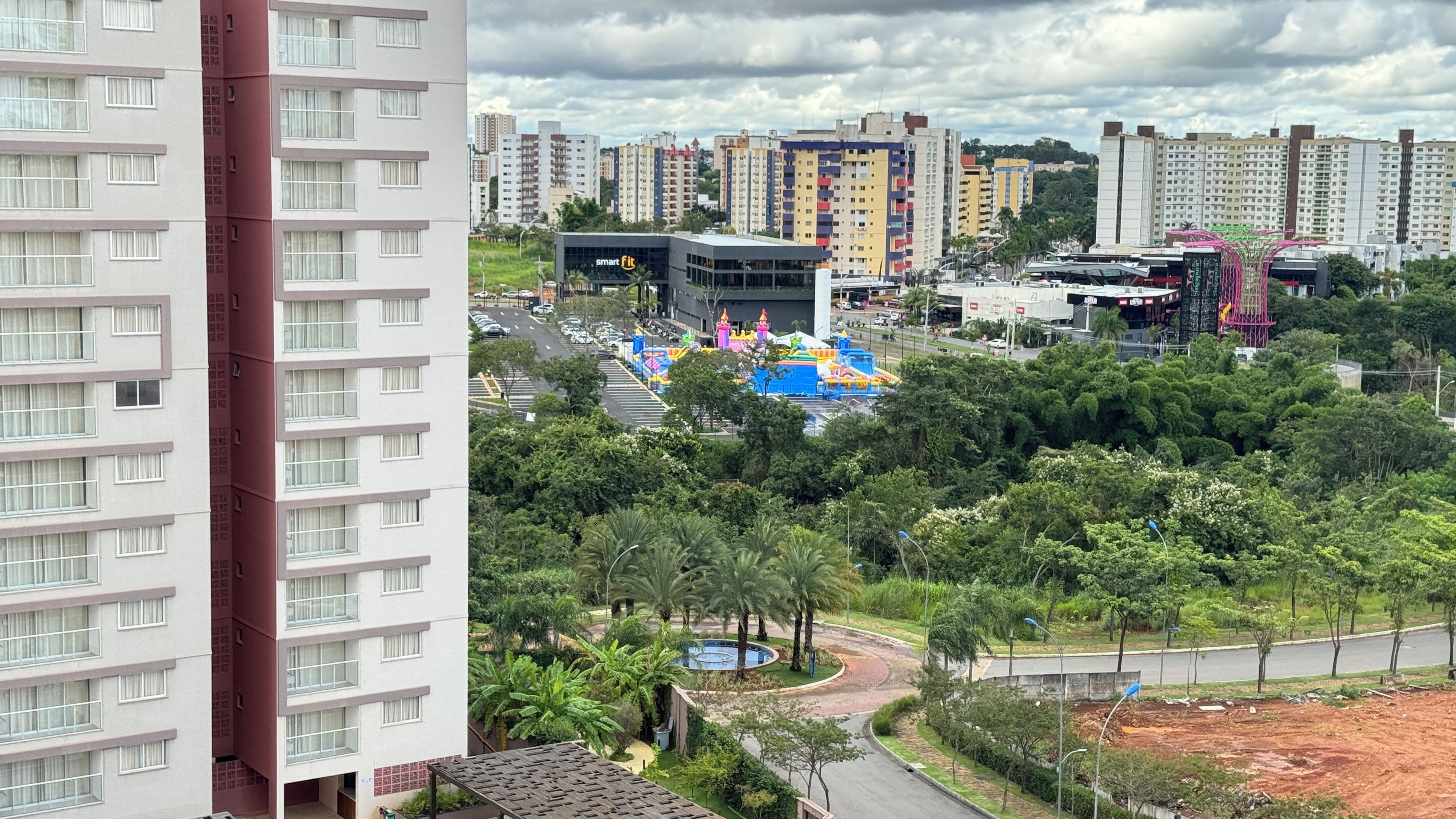 Un edificio residencial de varios pisos con diseño moderno, un área ajardinada con árboles y un parque infantil al fondo.