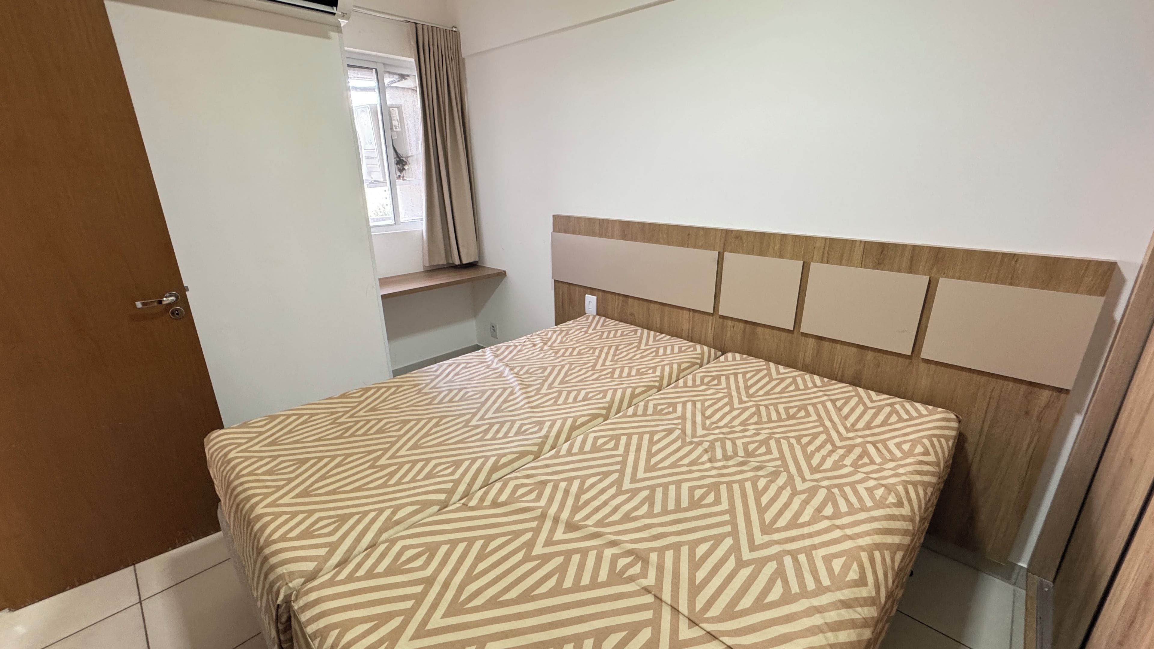 A bedroom with a bed, a wooden headboard, a window with curtains, and a door.