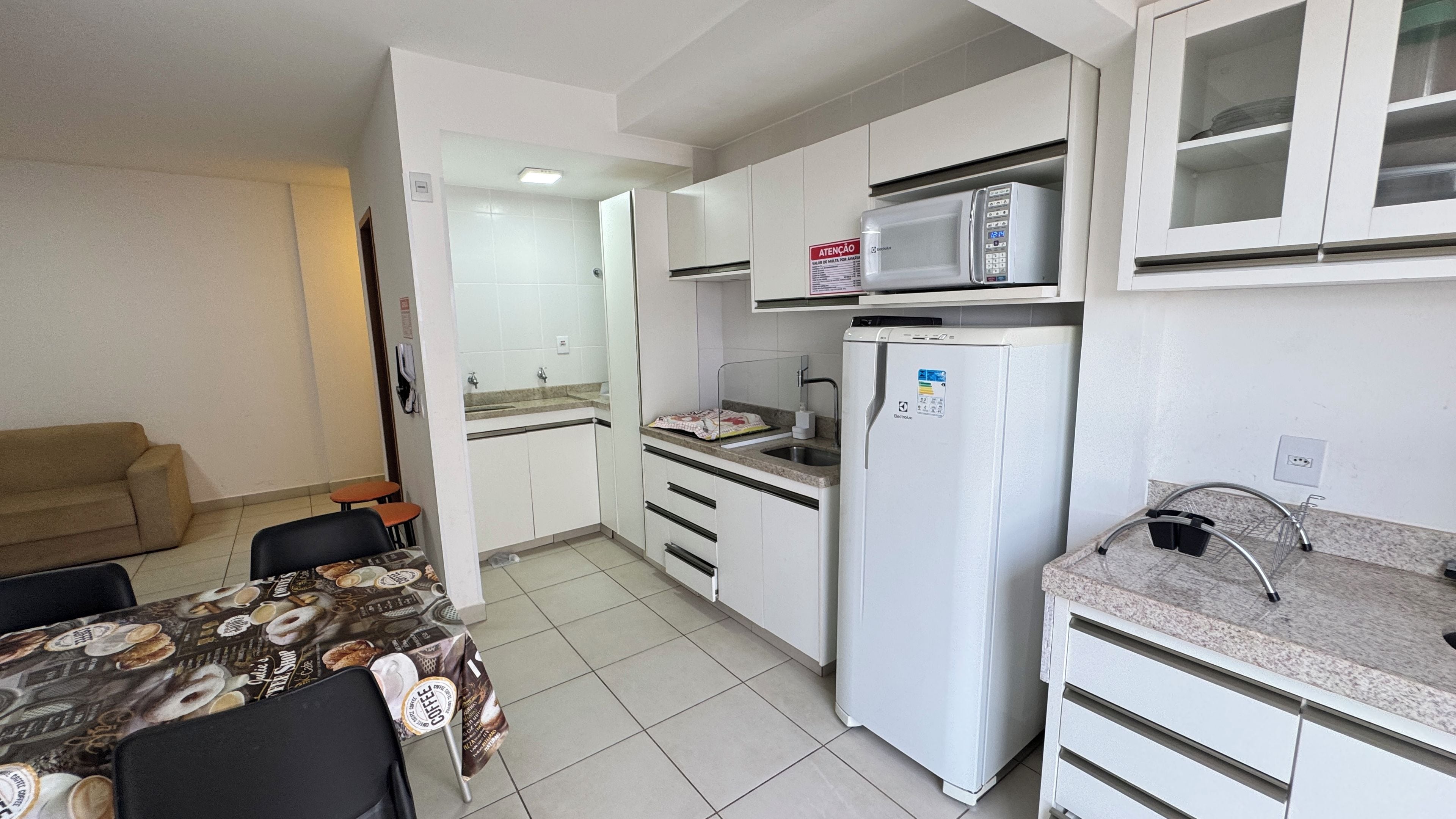 A compact kitchen with white cabinets, a refrigerator, a microwave, and a sink. There is a dining table with chairs and a coffee table.