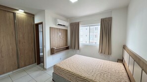 Un dormitorio con cama, armario y ventana con cortinas.