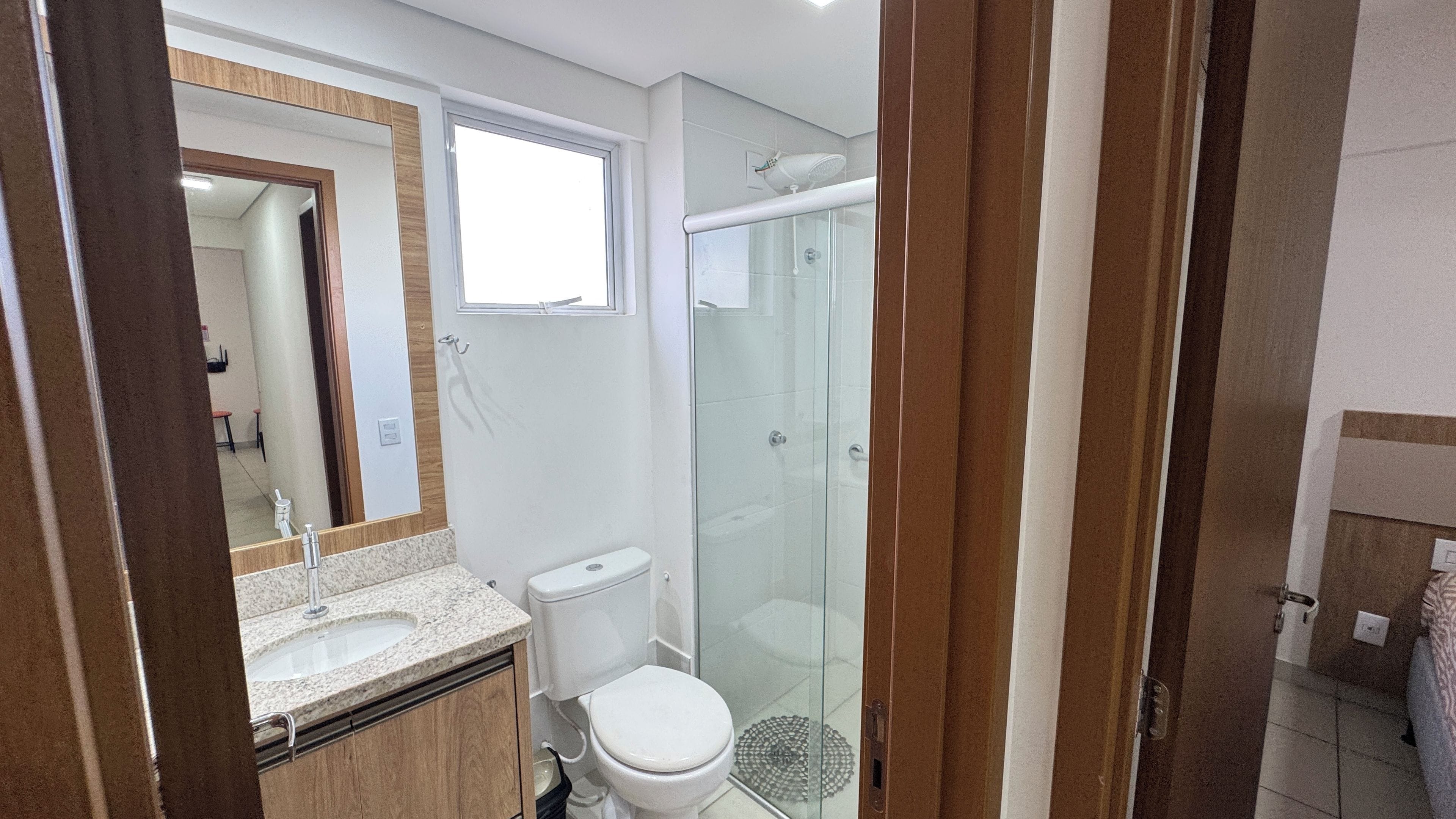 Casa de banho com cabine de duche em vidro, lavatório com bancada de mármore e sanita.